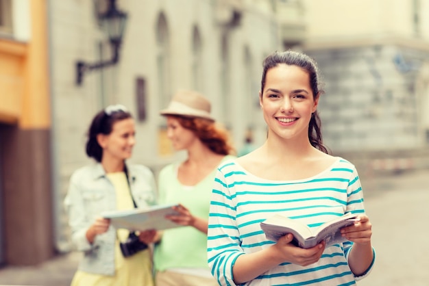 tourism, travel, holidays and friendship concept - smiling teenage girls with city guide, map and camera outdoors