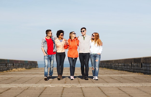 tourism, travel, people and friendship concept - group of happy teenage friends walking along city street and talking