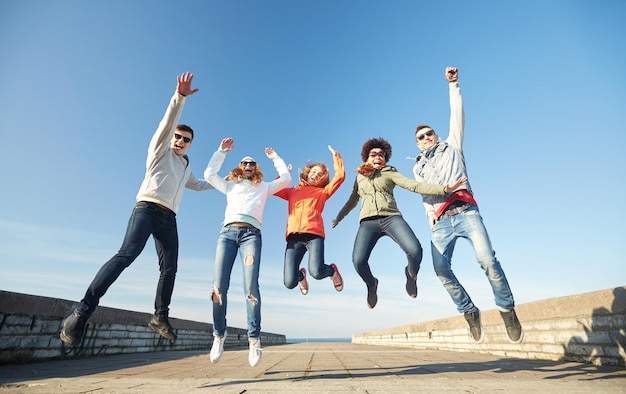 tourism, travel, people, leisure and teenage concept - group of happy friends in sunglasses hugging and laughing on city street