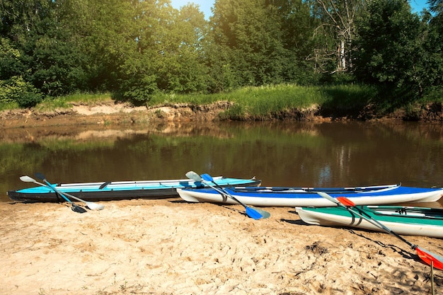 Tourist canoes with paddles stand on the river coast in summer on a water hike Rafting on inflatable and frame double and triple kayak boats family trip extreme adventure in summer