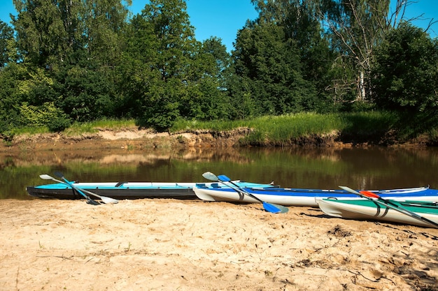 Tourist canoes with paddles stand on the river coast in summer on a water hike Rafting on inflatable and frame double and triple kayak boats family trip extreme adventure in summer