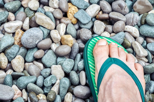 Tourist foot in bright green flipflops stands on pebble beach near sea