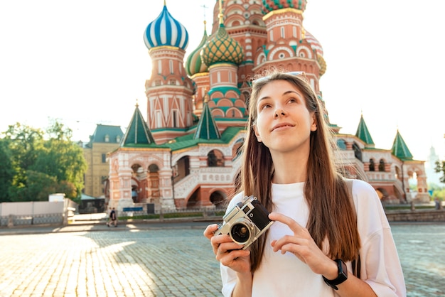 A tourist girl with a camera smiles on a sunny day against the background of St. Basil's Cathedral