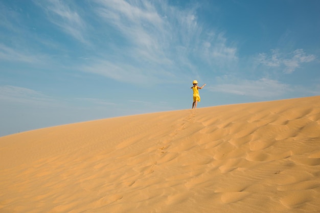 A tourist girl in a yellow dress runs along a sandy dune in the desert Travel sights of Dagestan Sarykum dune