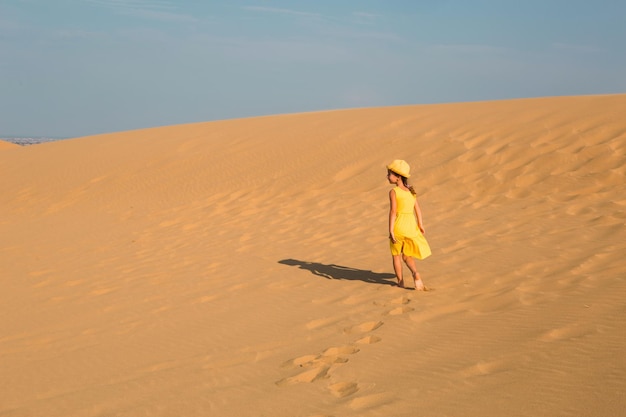 A tourist girl in a yellow dress runs along a sandy dune in the desert Travel sights of Dagestan Sarykum dune