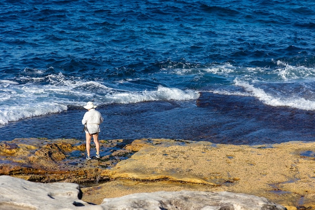 Tourist in hat standing with fishing rod in hand 