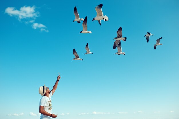 Tourist male feeding flock of seagulls on the beach against blue clea sky