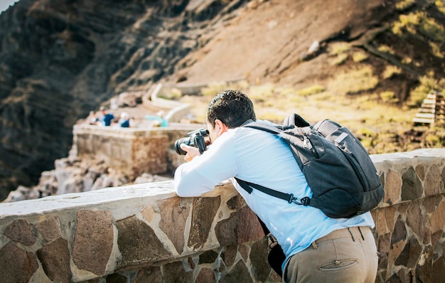 A tourist man with a photo camera taking photos at a viewpoint Adventurous man with his camera taking photos at a viewpoint Close up of tourist man taking photos at a volcanic viewpoint