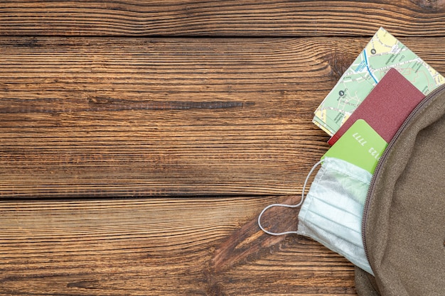 Tourist map, credit card, passport, protective mask stick out of travel backpack on wooden