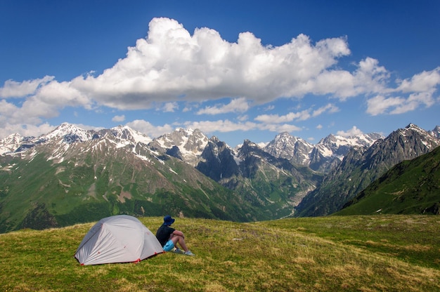 A tourist sits near his gray tent in the Caucasus Mountains of Georgia