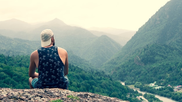 The tourist sits on a rock with a beautiful view of the mountains