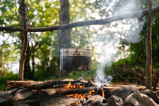 a tourist sootcovered bowler hat hangs over a smoking campfire at a forest camp in summer time