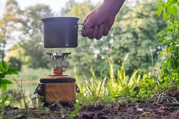 Tourist stove gas for camping and recreation against the backdrop of nature and the lake A man cooks food outdoors