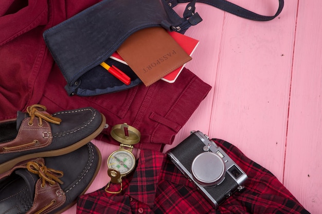 Tourist stuff bag jeans passport camera compass shoes shirt note pad on pink wooden background