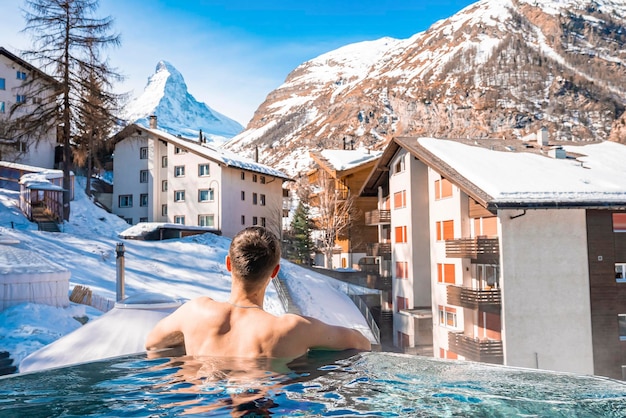 Tourist swimming in pool while looking at snow covered mountain and houses