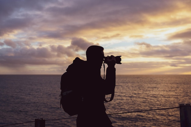 Tourist taking a picture on the cliffs of Boca do Inferno at sunset