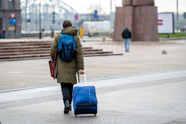 A tourist with a backpack pulls a suitcase on wheels down the street rear view