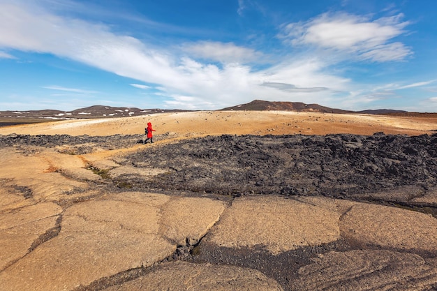 A tourist woman in a red jacket walks along a volcanic plateau in Iceland.