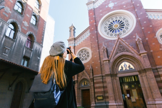 Tourist woman taking travel picture with camera of church during autumn holidays