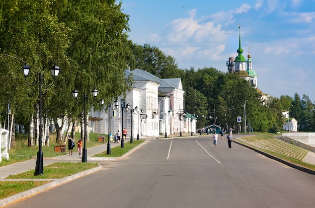 Tourists wallk on embankment of river Suhona and church of St. Nicolas in summer. Veliky Ustyug. Russia