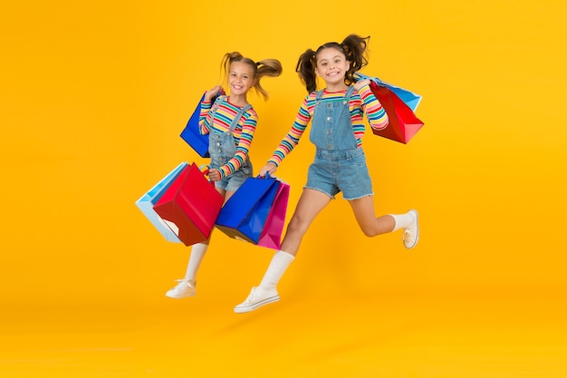 Towards purchase. Modern fashion. Kids fashion. Cute children hurry up for sale season. Discount and sale. Little girls carry shopping bags. Matching outfits. Trendy and fancy. Fashion shop.