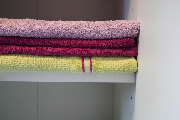 Towels on a shelf in a white cabinet Clean ironed pink and yellow towels folded in a pile Organization of household items in the bathroom or closet The result of the work of a housewife