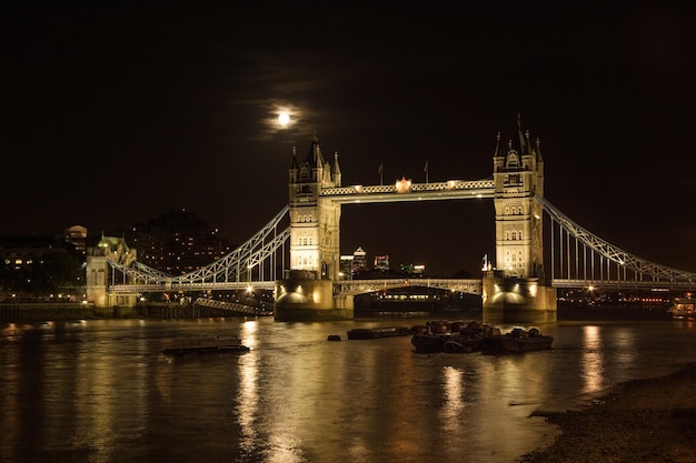 Tower bridge, full moon above, with river Thames illuminated in the night. London, United Kingdom