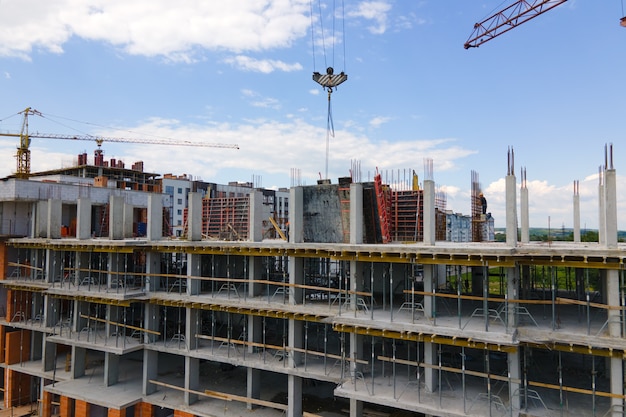 Tower crane at high concrete residential building under construction. Real estate development concept.