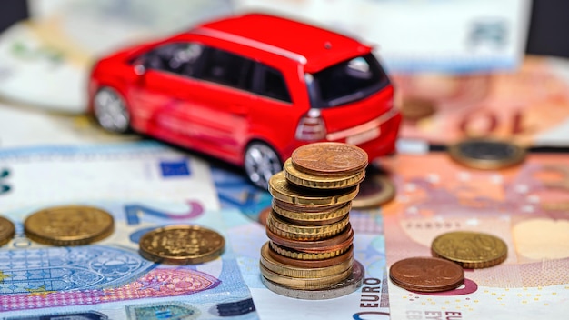 Tower with euro coins on the background of banknotes and red toy car insurance and loan concept