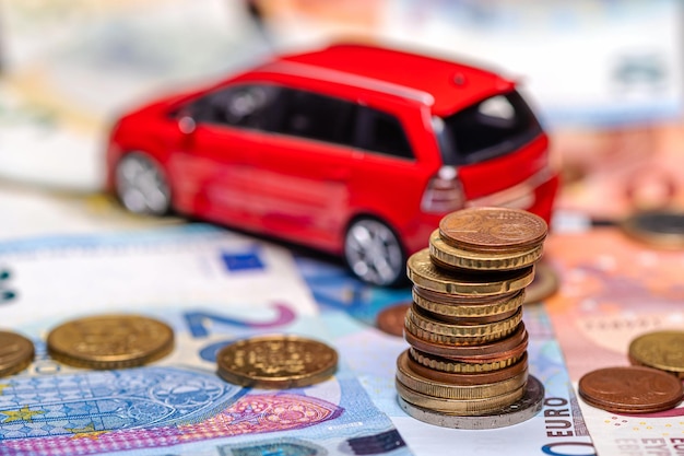 Tower with euro coins on the background of banknotes and red toy car insurance and loan concept