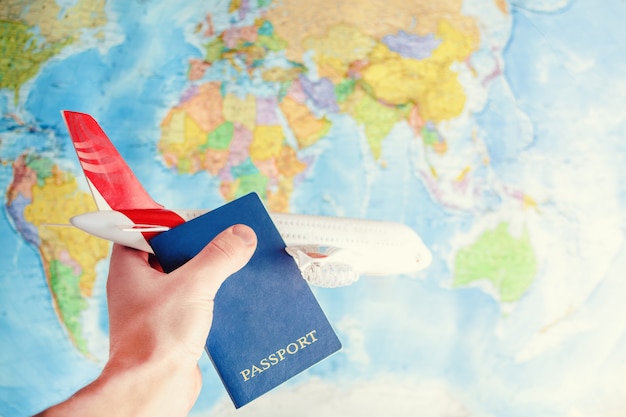 A toy airplane and a passport in hand on the background of a world map.