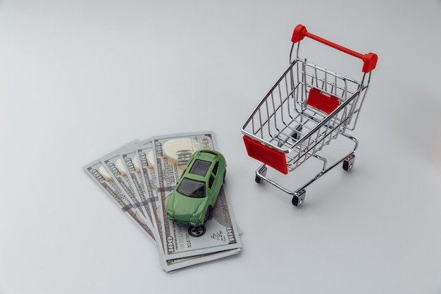 Toy car in a shopping basket and dollar banknotes on a white background.