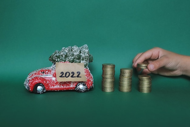 Toy car with christmas tree, new year number 2022 and financial savings, dream of a new car. Green background