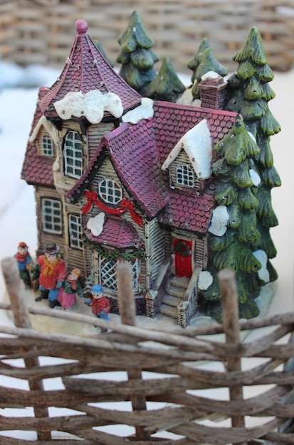 A toy diorama of small house in a winter setting surrounded by a wattle fence