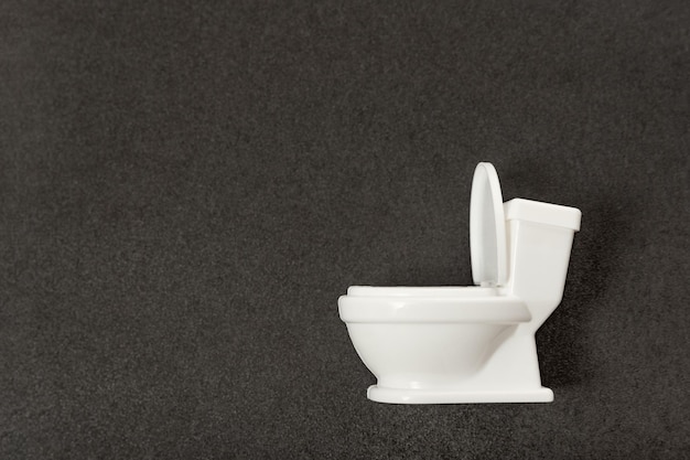 Toy little white toilet bowl on gray background Side view on toilet model Restroom or WC Space for text