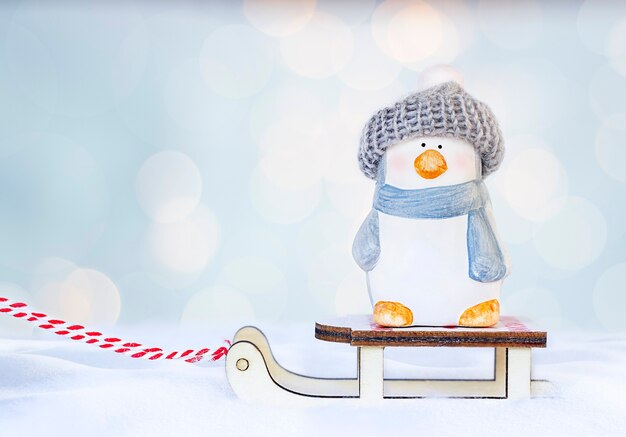 a toy penguin in a hat stands on a sled in the snow