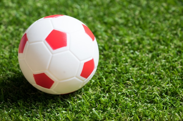 Toy red and white color football on artificial green grass background