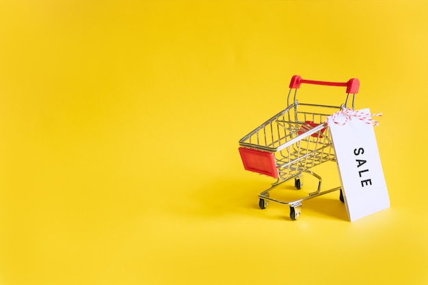 Toy supermarket cart with sale sticker on a yellow .  sales, shopping and black friday. Copyspace for text.