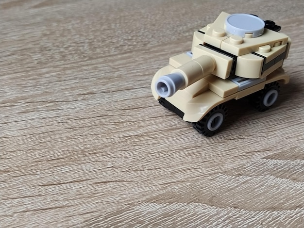 Photo toy tank on a wooden table plastic toy craft from a childrens designer the beige color of the tank a defocused image around the edges lesson that develops the fine motor skills