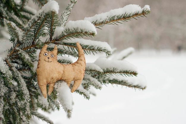 Toy tiger, cat, symbol of the eastern horoscope 2022, against the background of a snowy Christmas tree. Snowing. Blurred winter background. The concept of the coming New Year.