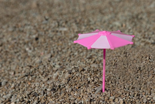 Toy umbrella in pink and white colors on the beach by the sea Selective focus