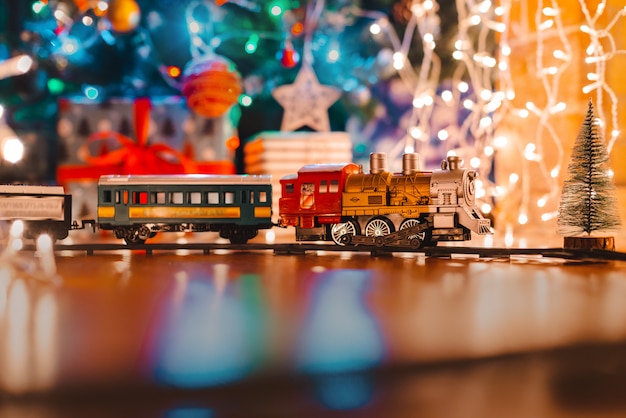 Photo toy vintage steam locomotive on the floor under a decorated christmas,  bokeh lights garland.