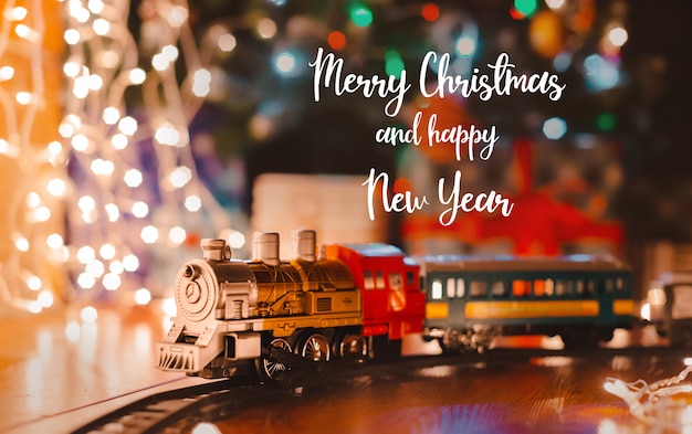 Photo toy vintage steam locomotive on the floor under a decorated christmas tree on a   bokeh lights garland.