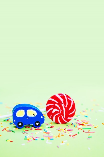 Toy wooden blue car and lolipop with confetti on green