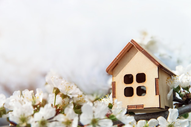 Toy wooden house and cherry flowers Spring natural background and copy space Blooming tree Concept of mortgage construction rental family and property