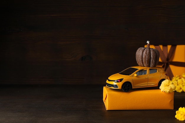 Toy yellow car with a gift pumpkin and flowers place for text