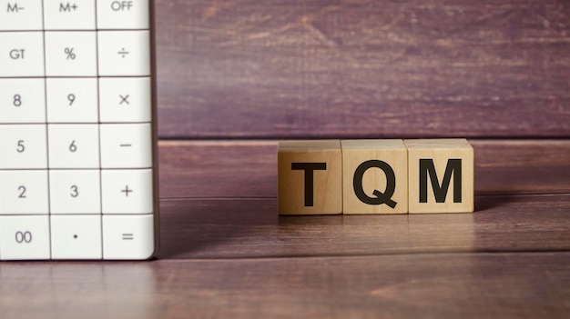 TQM text on wooden block with calculator on wooden background