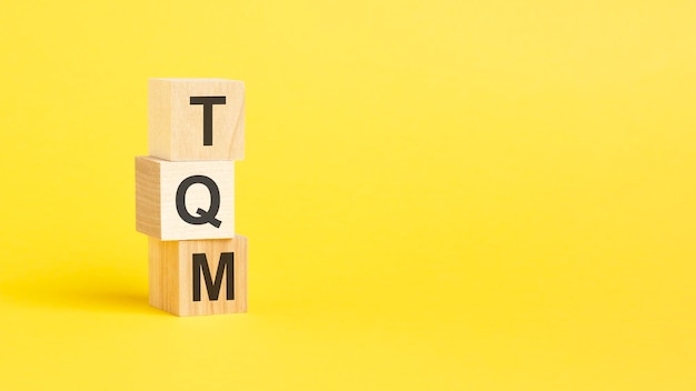 TQM Total Quality Management text on wooden block with yellow background