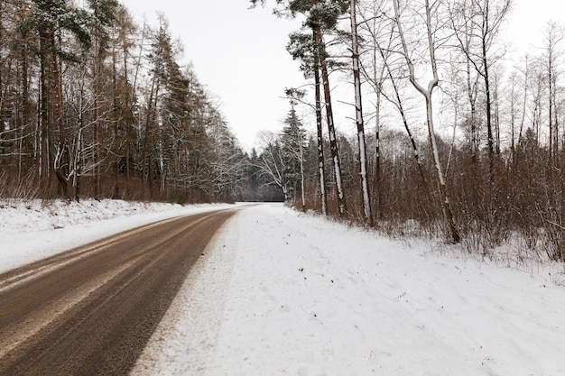 Traces left by car on the snow-covered road in the winter season. Photo closeup in cloudy weather. The road passes through the forest with trees