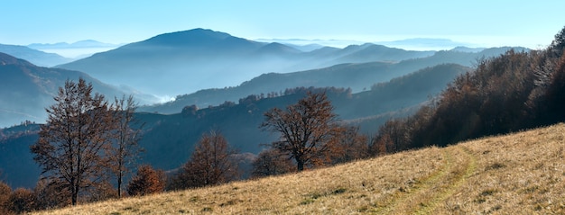 Traces of wheels on slope.  Autumn misty mountain panorama.